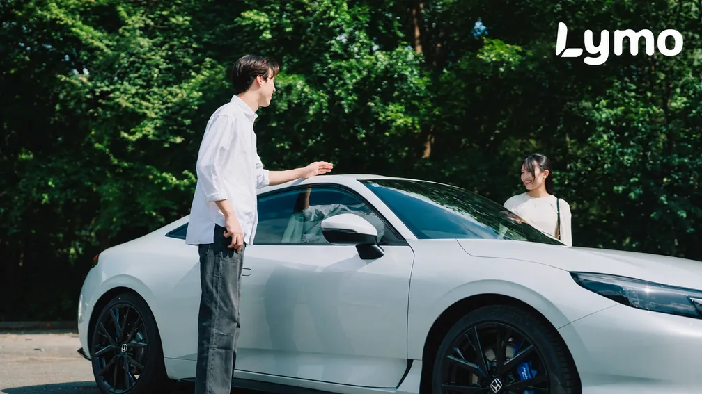 緑に囲まれた白い車と二人の実写写真に、白いLymoロゴを重ねたビジュアル
